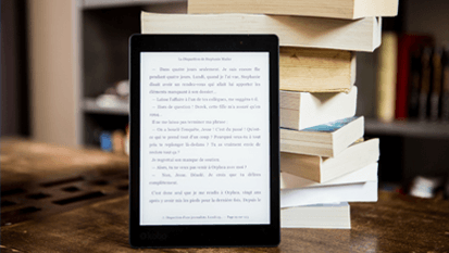 An eBook page displayed in a tablet placed against vertical stack of books on a table.