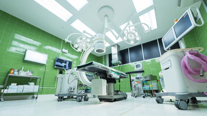 Inside view of a modern operating theatre with overhead surgical lights, monitors, screens, and medical equipment.