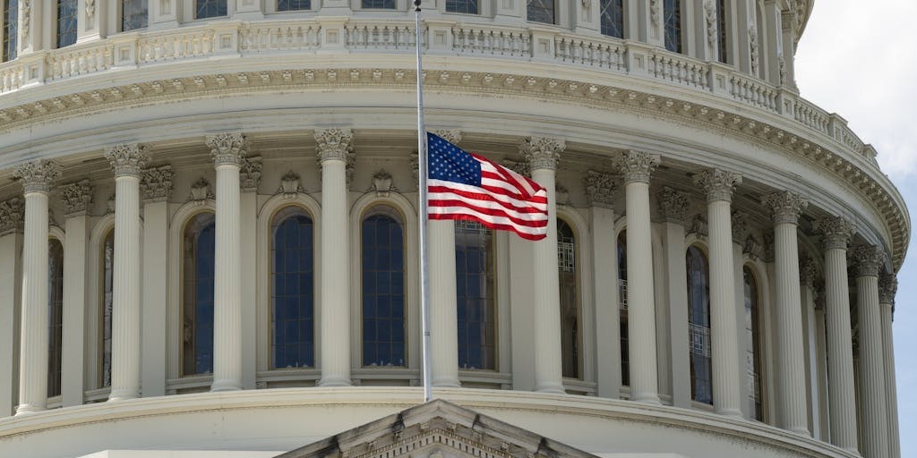 Close-up view of the U.S. Capitol building with an American flag flying at half-staff in front of its columns and arched windows.